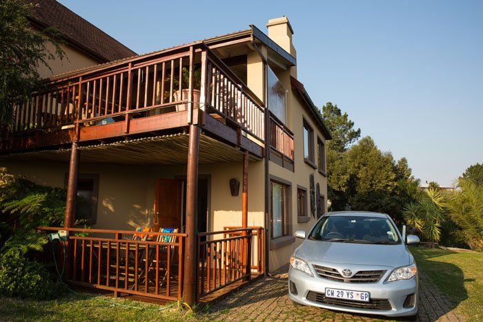 External shot of Panorama Lodge featuring wooden balconies and a silver Toyota parked alongside it. Knysna, South Africa.