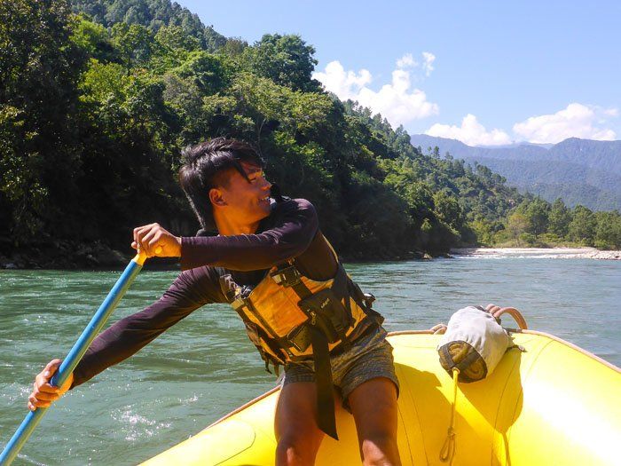 A local guide from Punakha, paddling at the back of the raft, smiling and looking behind him at the river.