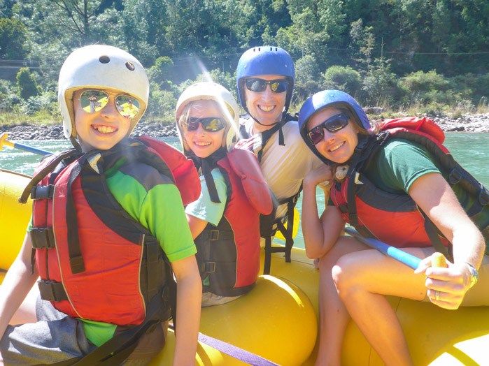 The Earth Trekkers family sitting in a yellow raft, wearing red life jackets, helmets, sunglasses and smiling at the camera.