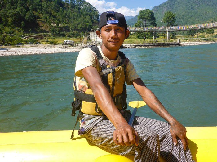 A local guide from Punakha, sitting on the edge of a yellow raft, wearing a baseball cap and a yellow life jacket.