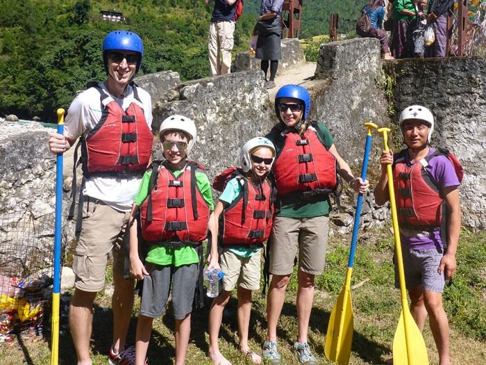 The Earth Trekkers ready to white water raft, wearing red life jackets, helmets and holding paddles.
