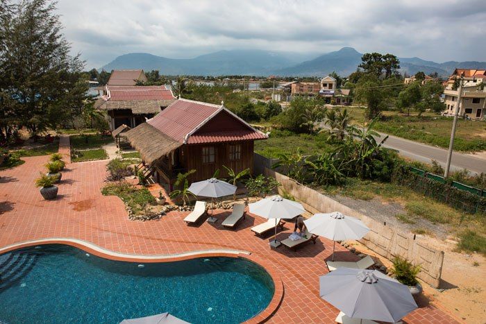 A view over the sunlounges and the pool with mist mountains in the background at the Two Moons Hotel in Kampot in Cambodia.