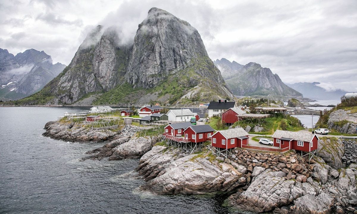 a small town on a rocky shore with mountains in the background with Lofoten in the background