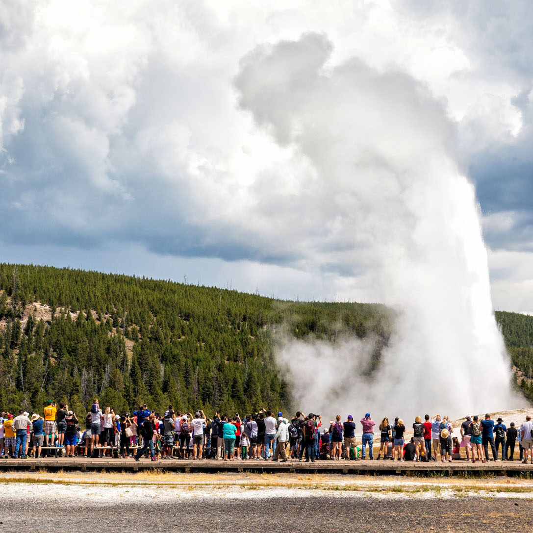 Old Faithful geyser erupting at optimal viewing time with fewer crowds in foreground