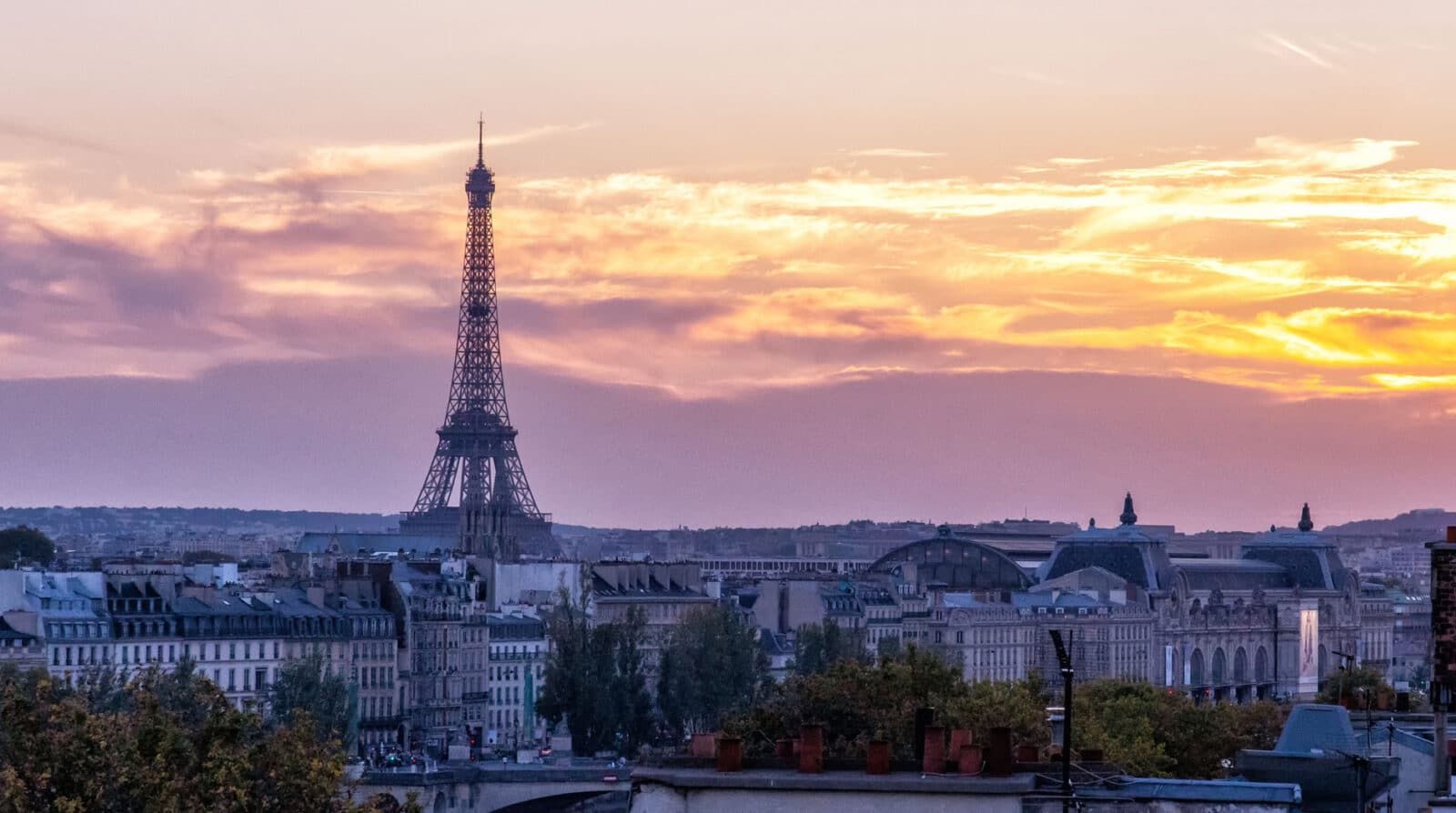 Eiffel Tower glowing at sunset above Paris rooftops